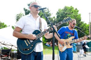 Musicians playing electric guitars on outdoor festival stage with sound equipment.