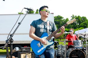 Guitarist in blue shirt performing with band at outdoor summer concert.