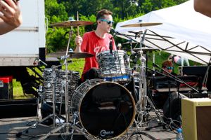 Drummer playing on Pearl drum kit at outdoor music festival.