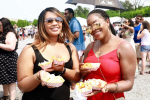 Two attendees hold colorful beverages and snacks at a summer food festival.