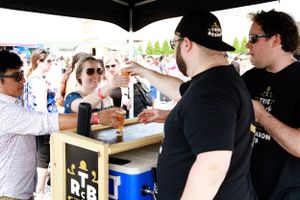 Vendors serving drinks to customers at an outdoor festival booth.