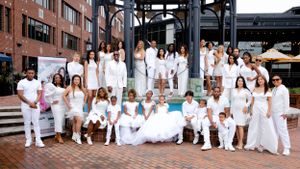 Large group wearing all-white outfits poses together on brick steps for formal photo shoot.