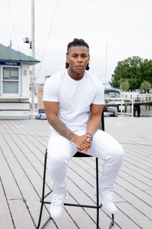 Athletic person in white outfit sitting on stool at wooden dock.
