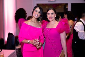Two women in bright pink formal dresses pose together at an evening event.