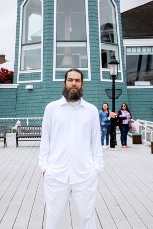 Person in white clothing standing in front of teal coastal building with large bay windows.
