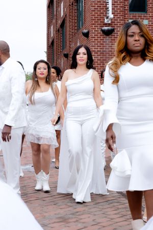 Group walking in coordinated white outfits along brick pathway near historic building.