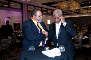 Two attendees examining paperwork at formal evening event with chandelier lighting.