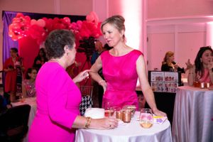Guests in pink attire converse at a round table during formal event.