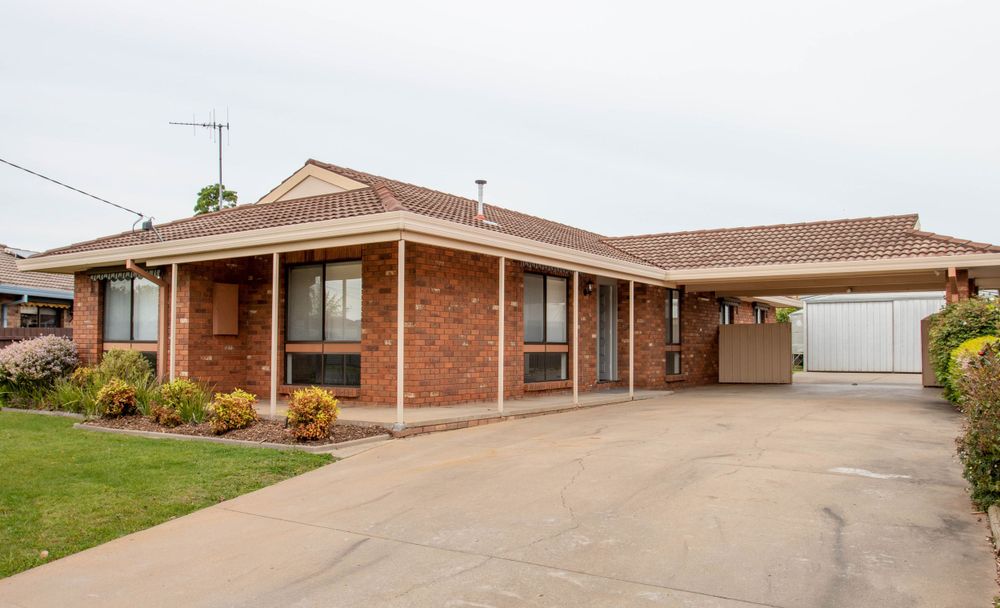 Single-story brick home with covered porch and well-maintained front lawn and garden beds.