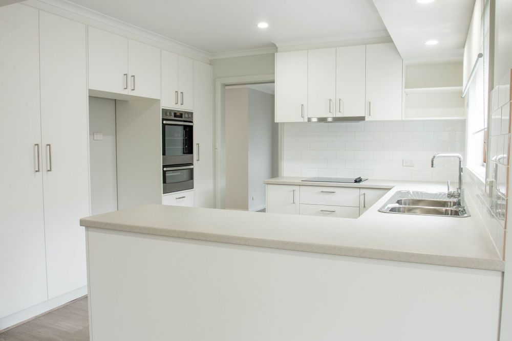 Contemporary white kitchen with built-in appliances and L-shaped counter layout.