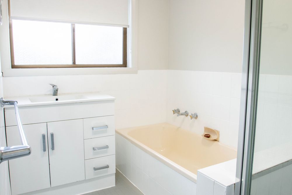 Clean white bathroom featuring built-in vanity and spacious bathtub beneath window.