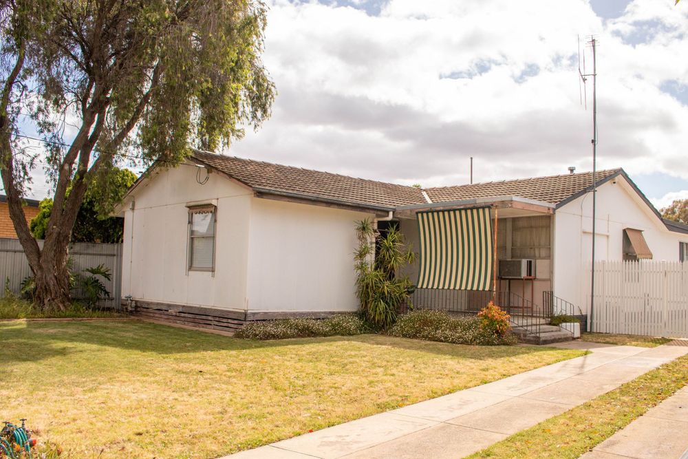 Small white ranch house with front yard and willow tree against cloudy sky.