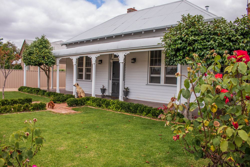 Charming white cottage-style house with arched entrance porch and colorful garden featuring red roses.