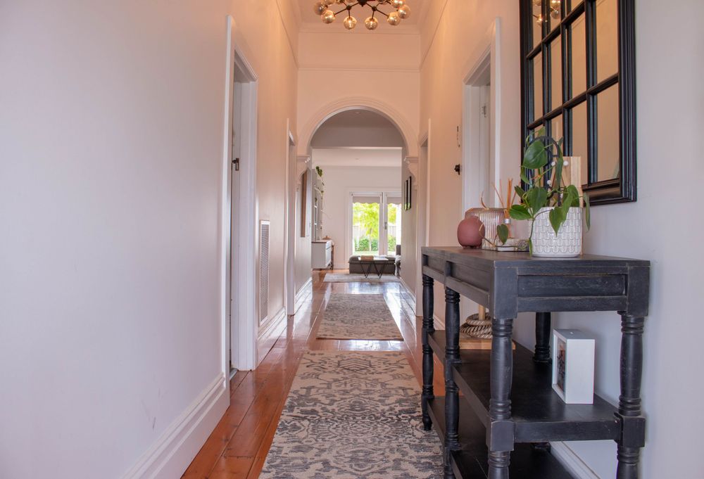 Elegant hallway with arched doorways, hardwood floors, and console table decorated with potted plants.
