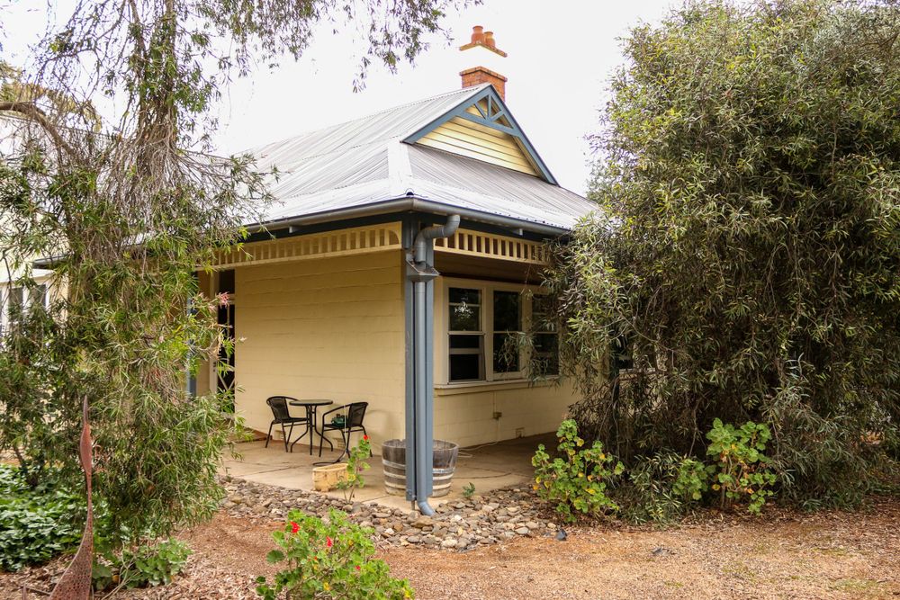 Charming cottage with wrap-around veranda and decorative trim surrounded by trees.