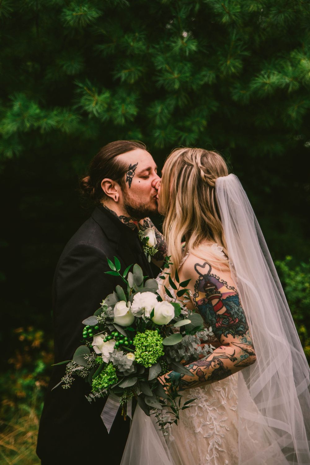 A romantic wedding couple shares a kiss while holding a white and green floral bouquet.