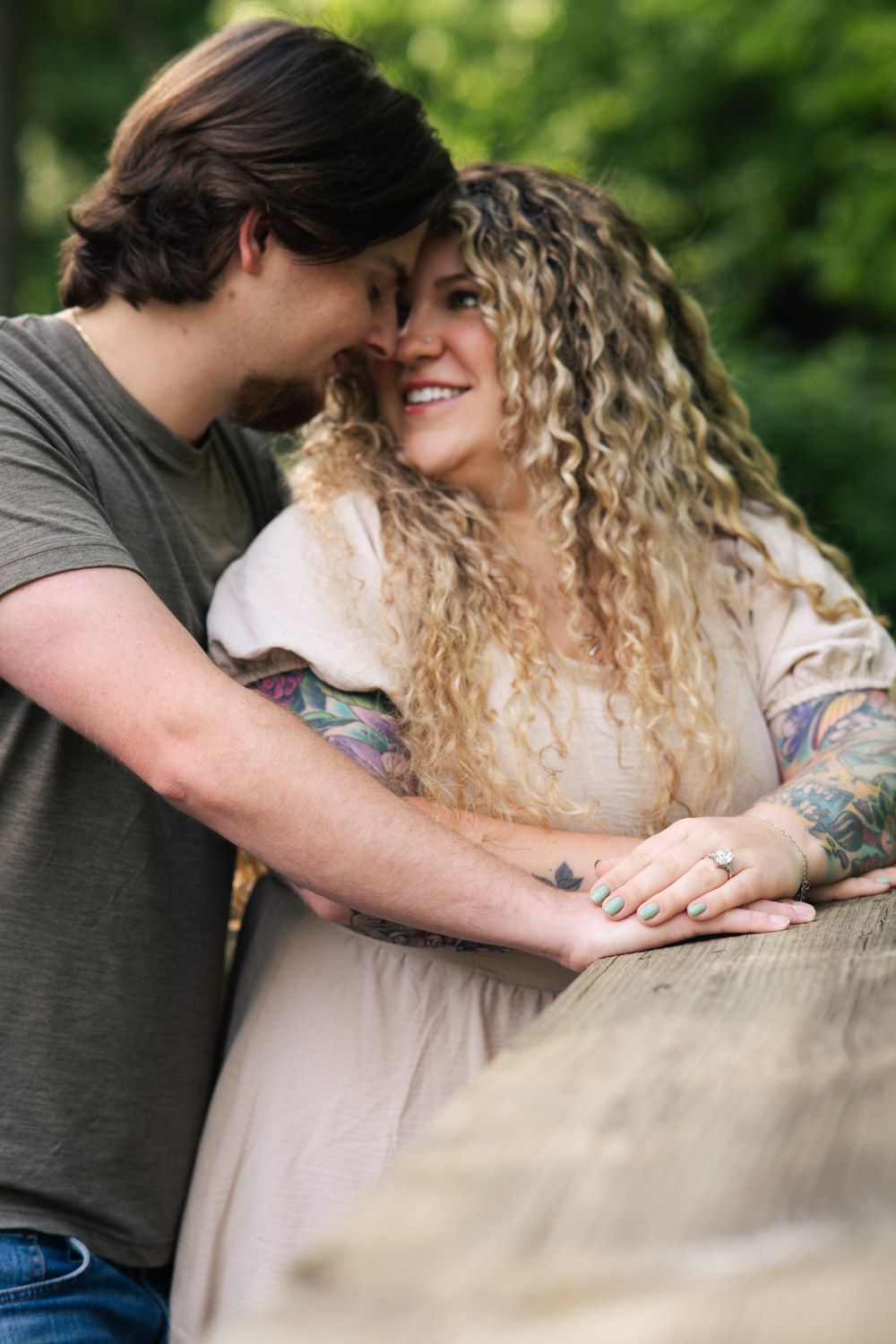 A romantic couple shares an intimate moment leaning against a fence outdoors with natural greenery in the background.