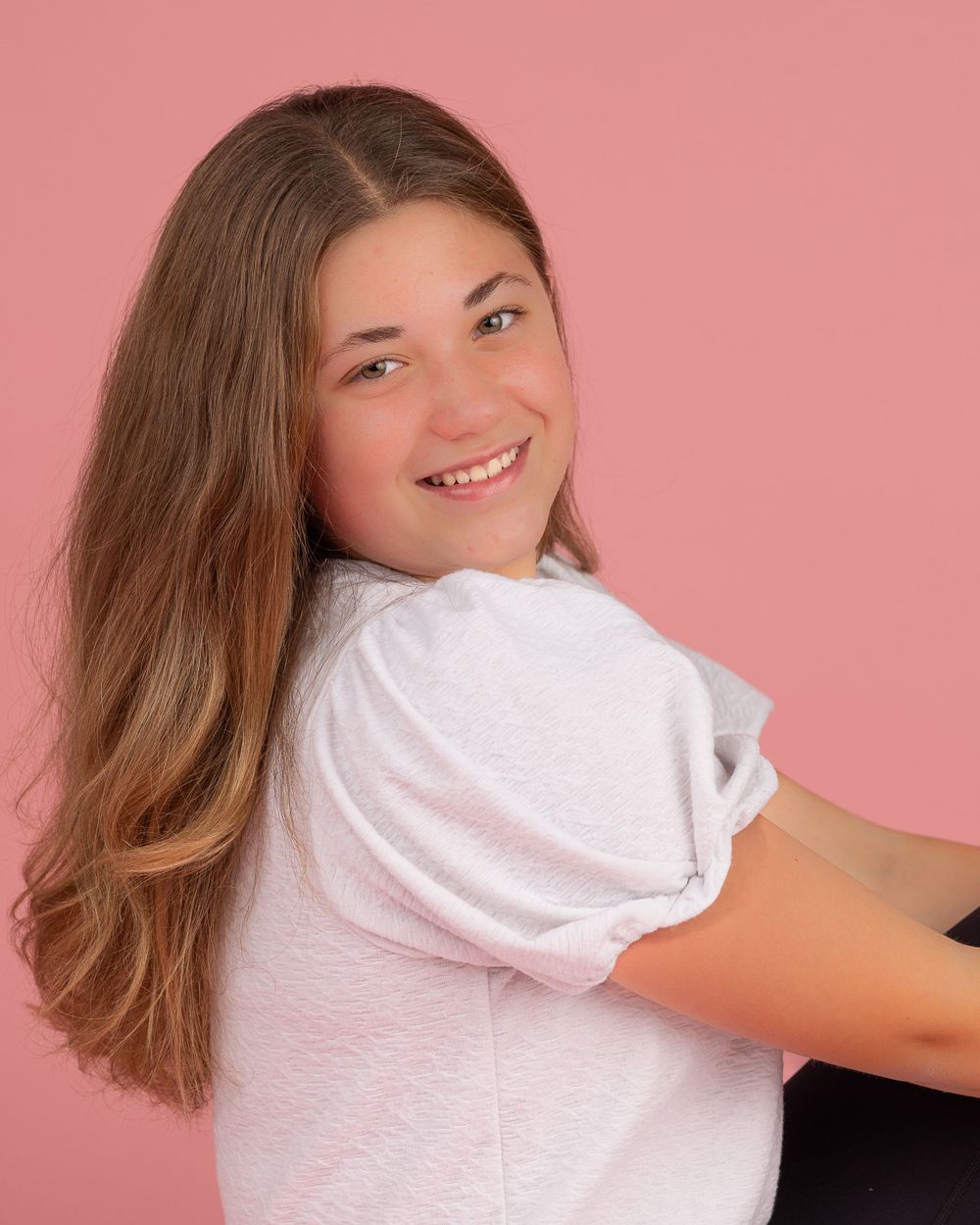Dynamic portrait of person in white top against pink background with flowing hair at home studio