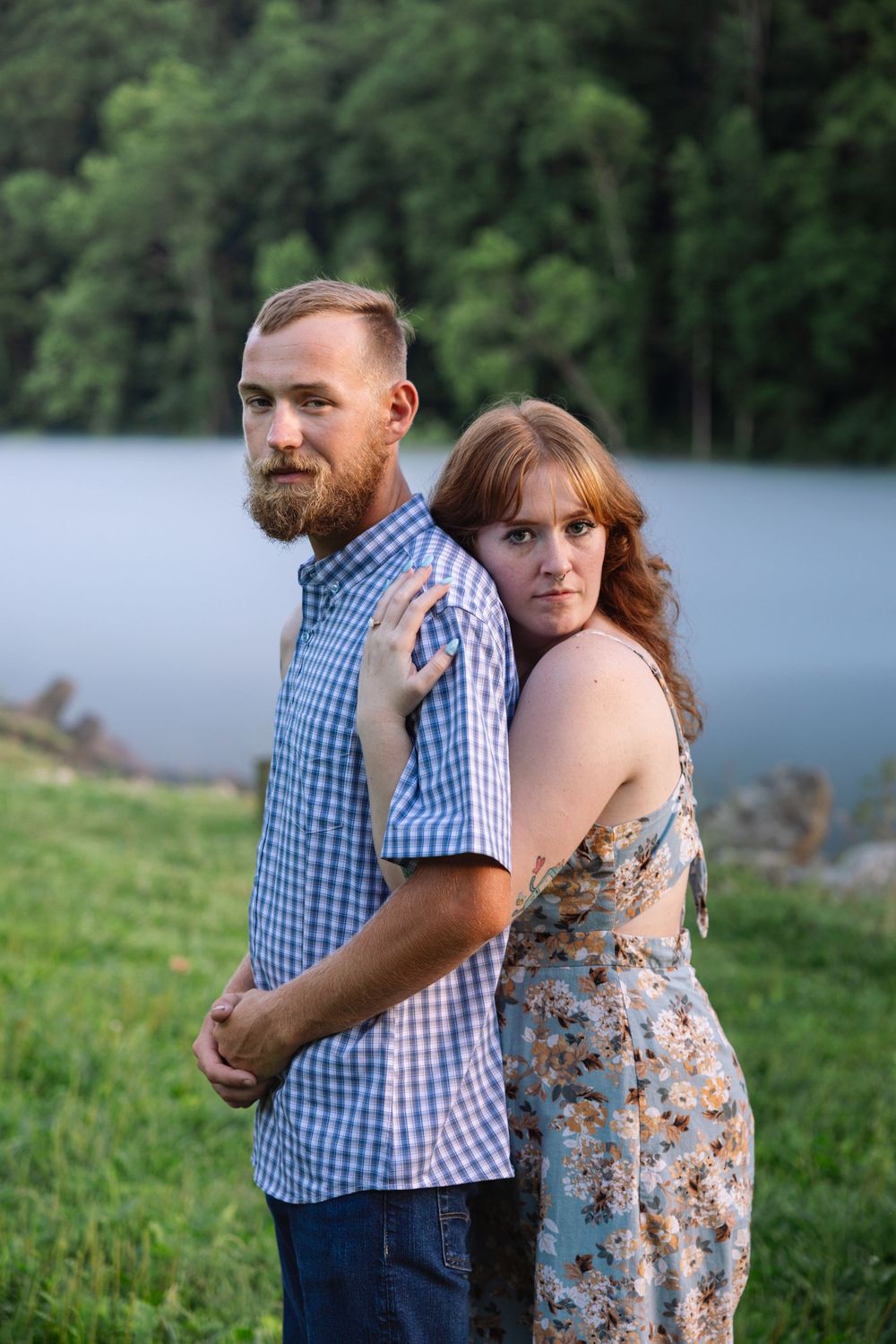 A couple shares an intimate moment by a serene lake while wearing casual summer attire.