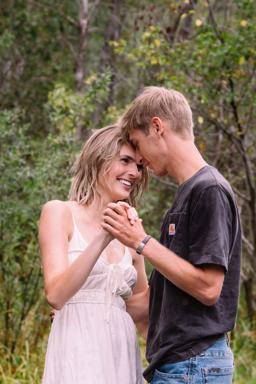 A tender moment between a couple dancing together in a natural outdoor setting surrounded by greenery.