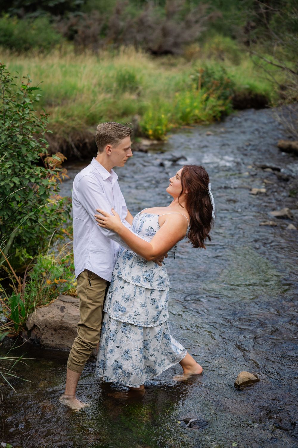 A couple enjoys romantic moments by a flowing stream on a summer afternoon, surrounded by greenery.
