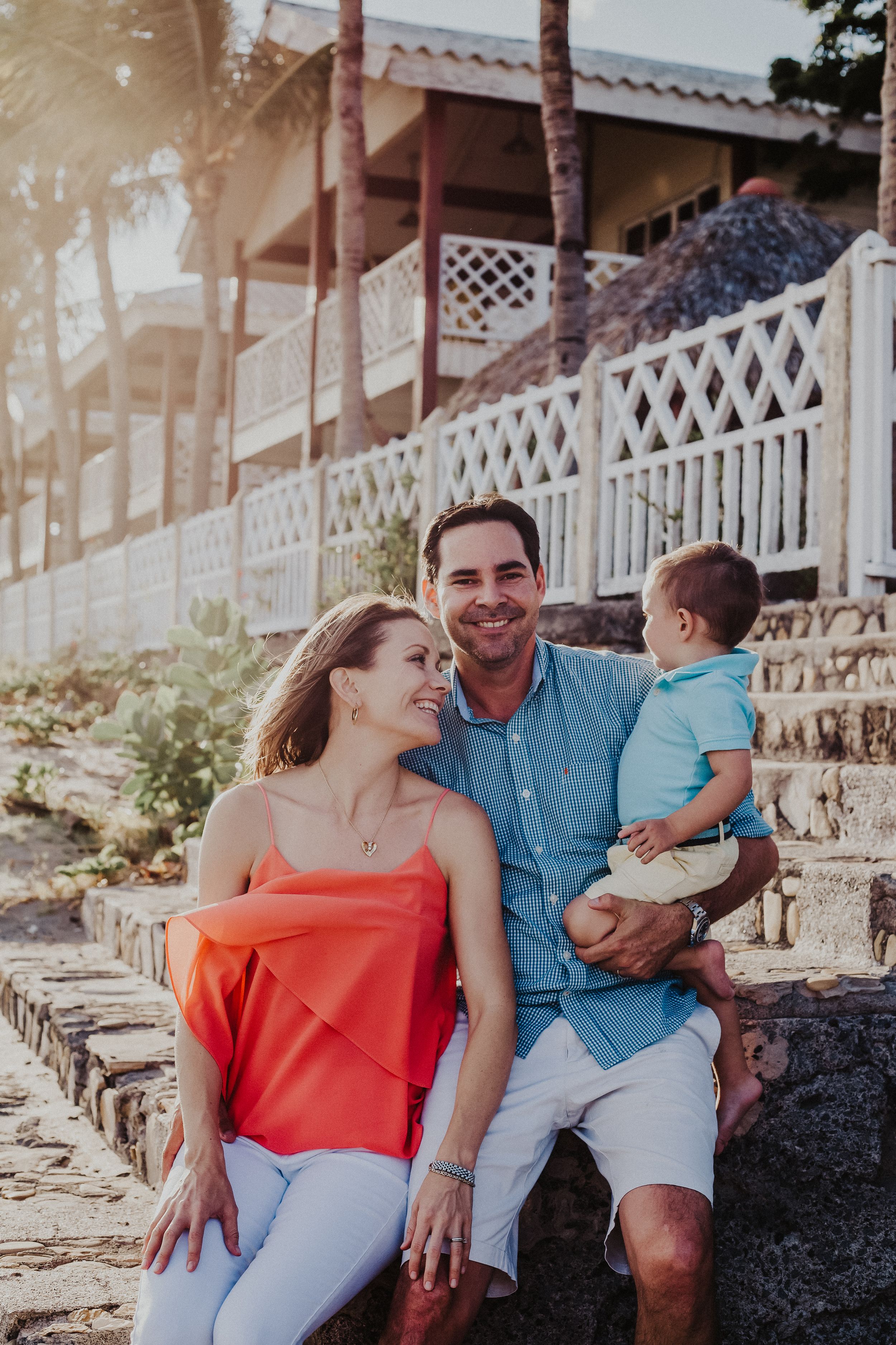 family of three sit on stairs on the beach while smiling