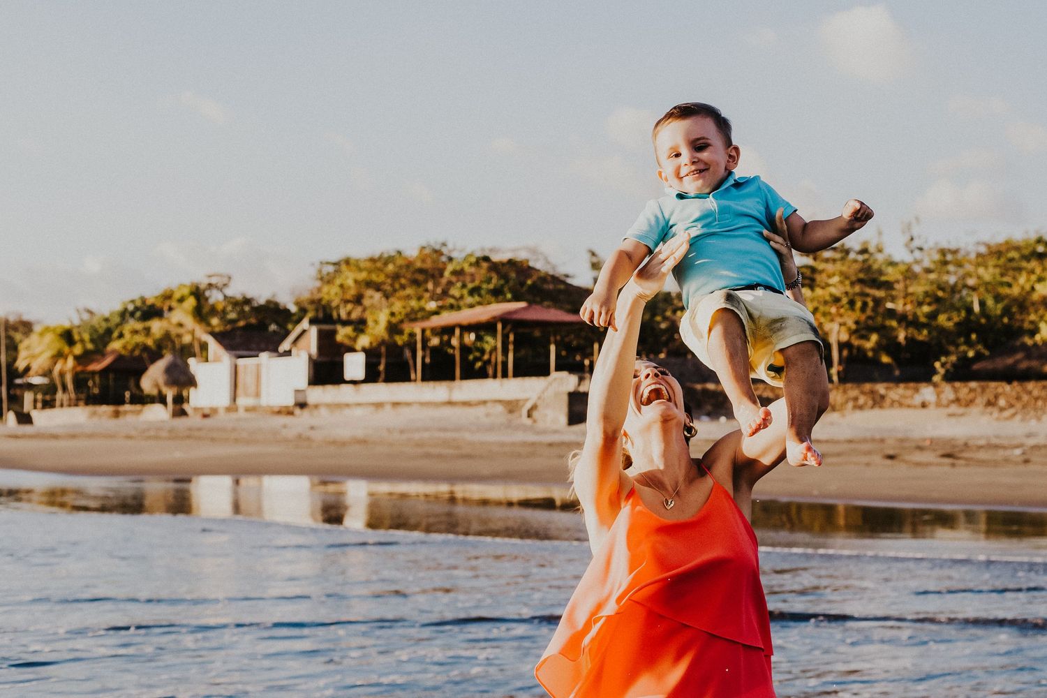 mother lifts son into the air over the water on the beach while laughing