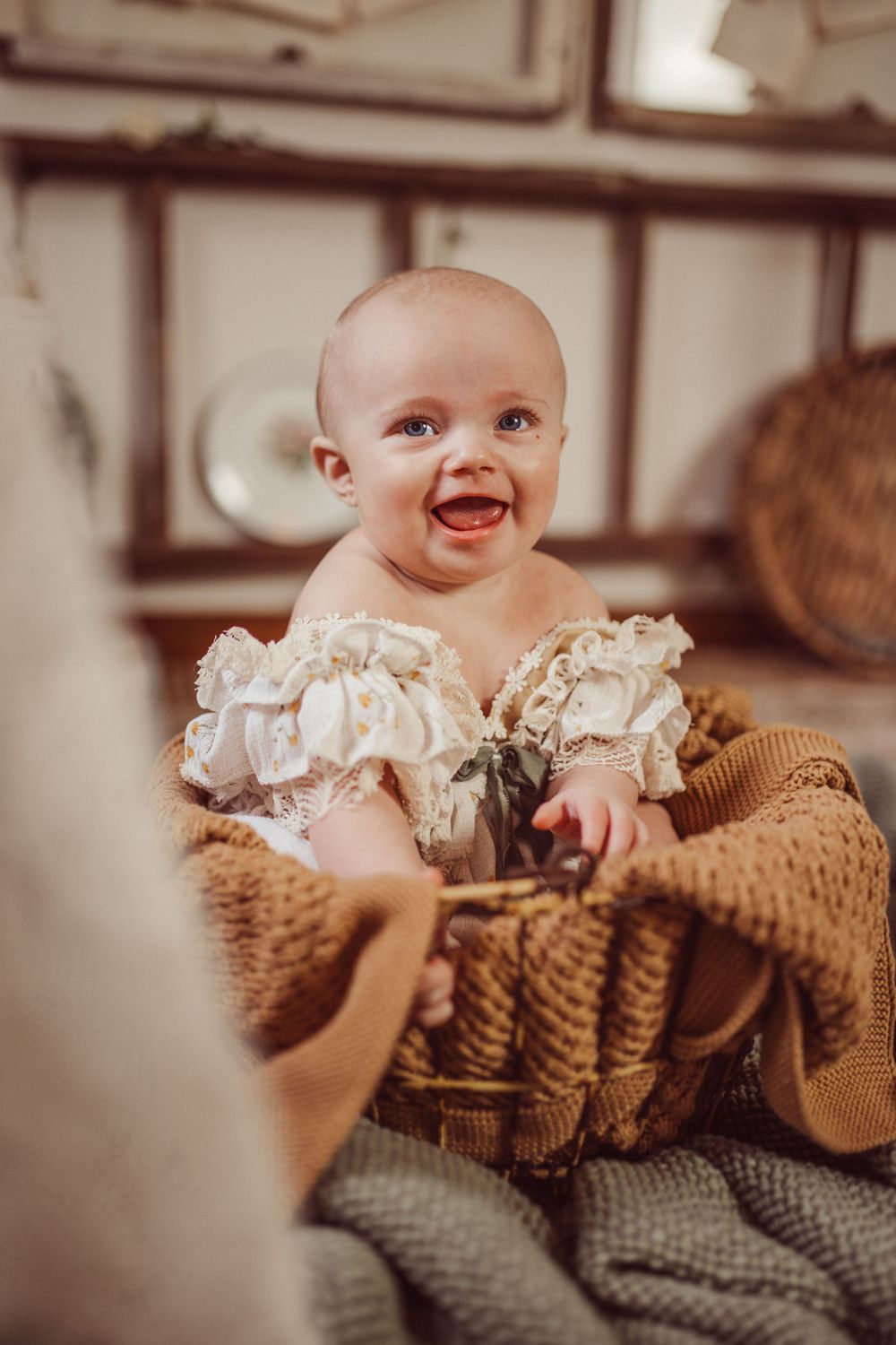 Happy baby wearing vintage lace outfit sitting in woven basket with knit blanket.