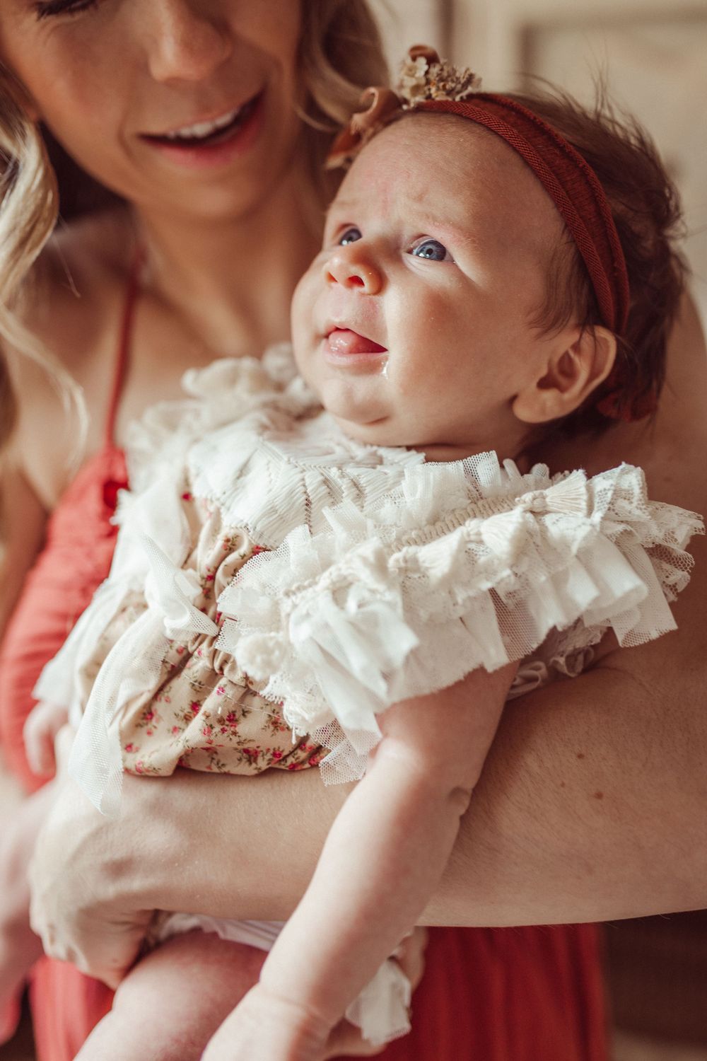 Baby in ruffled white dress and red headband being cradled in arms.