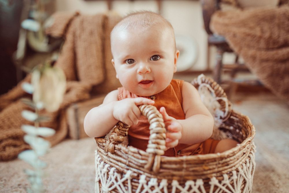 Happy baby sitting in decorative woven basket wearing orange outfit.