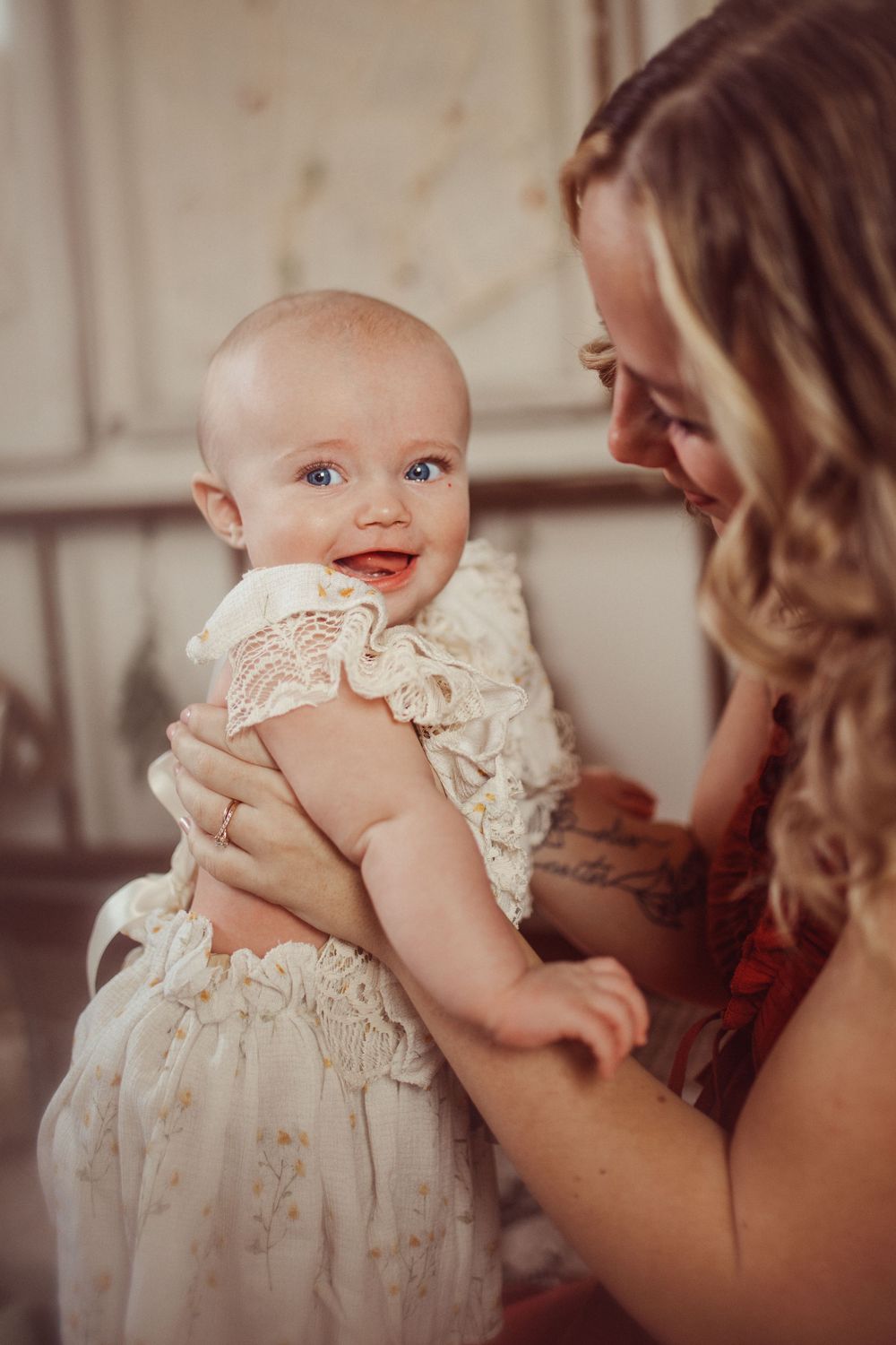 Warm toned portrait of sweet baby in white lace dress being held lovingly.