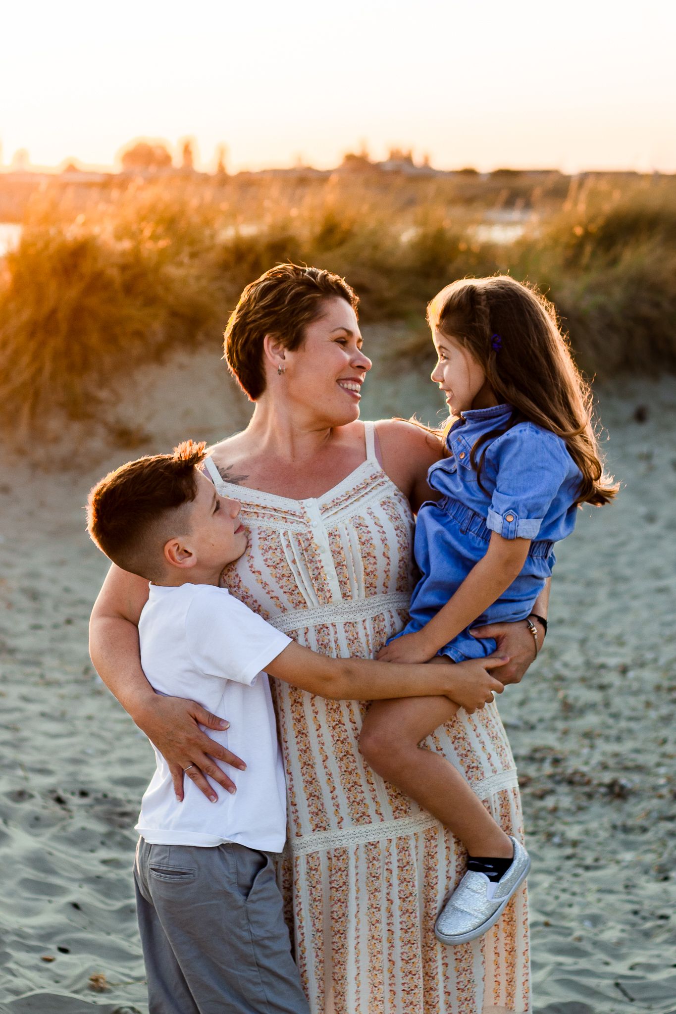 On a beach on Hayling Island a Mum smiles lovingly at her Son and Daughter while the Sun sets behind them.