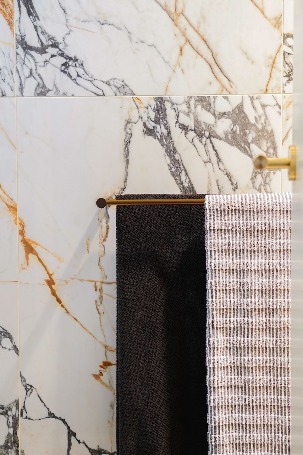 Close-up of marble tile bathroom wall with black and white striped towels on gold rack.
