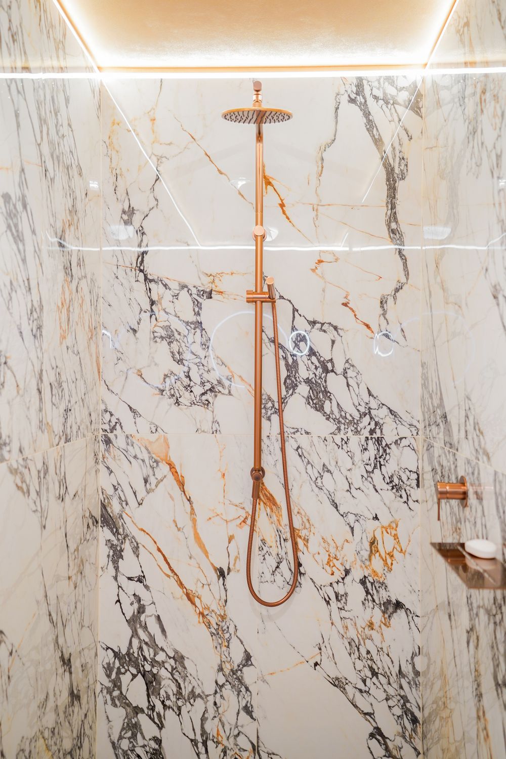 Luxurious marble shower with copper fixtures and dramatic veining pattern in white and gold.