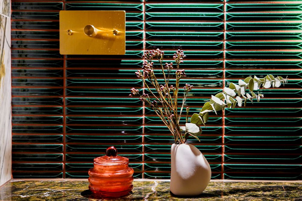 Decorative vignette featuring ceramic vase with dried flowers against green slatted backdrop.