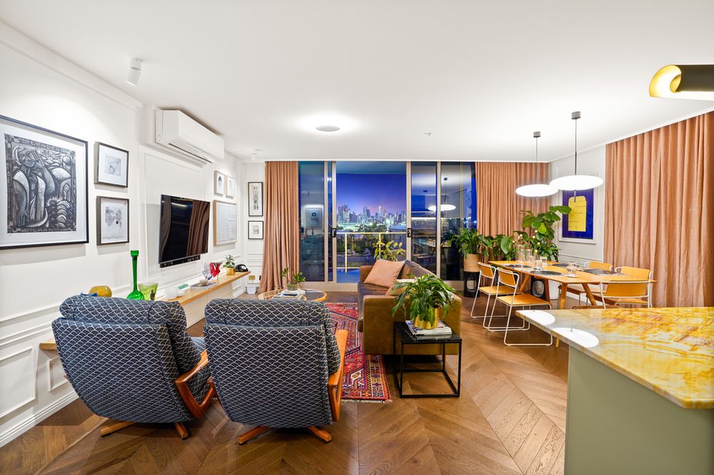 Modern living room with city views, wood floors, and comfortable seating area next to open kitchen.