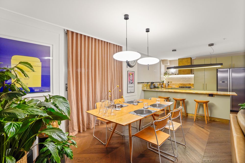 Open plan dining area with wooden table, modern chairs, and floor-to-ceiling windows beside kitchen space.