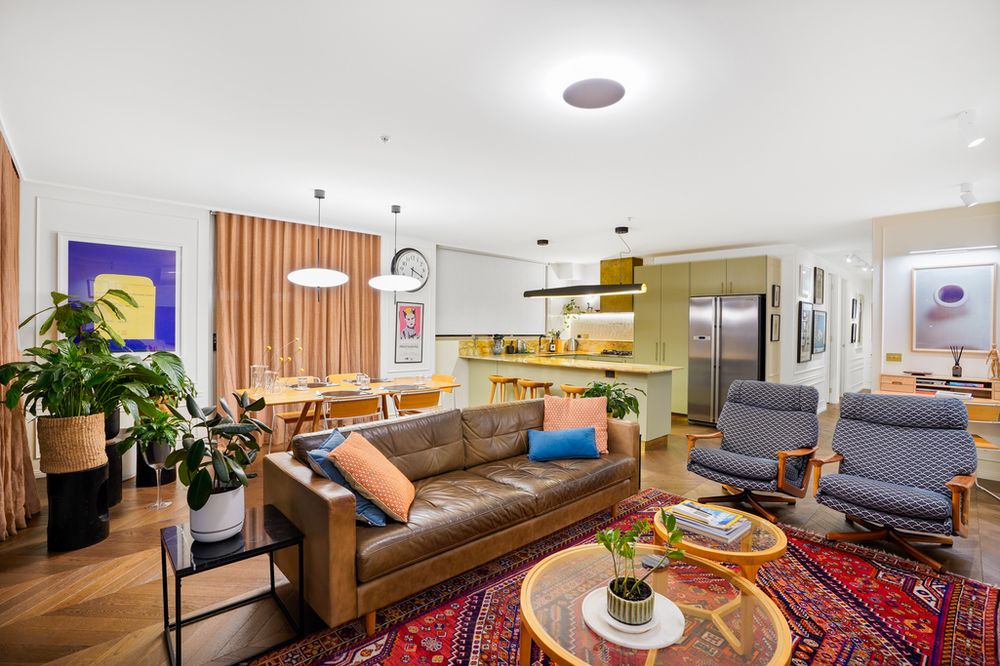 Modern open concept living room with leather couch, patterned rug, and wooden accent wall features stylish lighting fixtures.