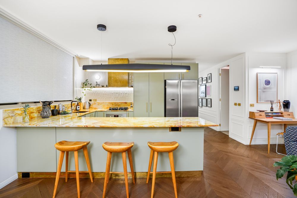 Modern white kitchen with wooden bar stools, stainless steel appliances, and yellow accents.