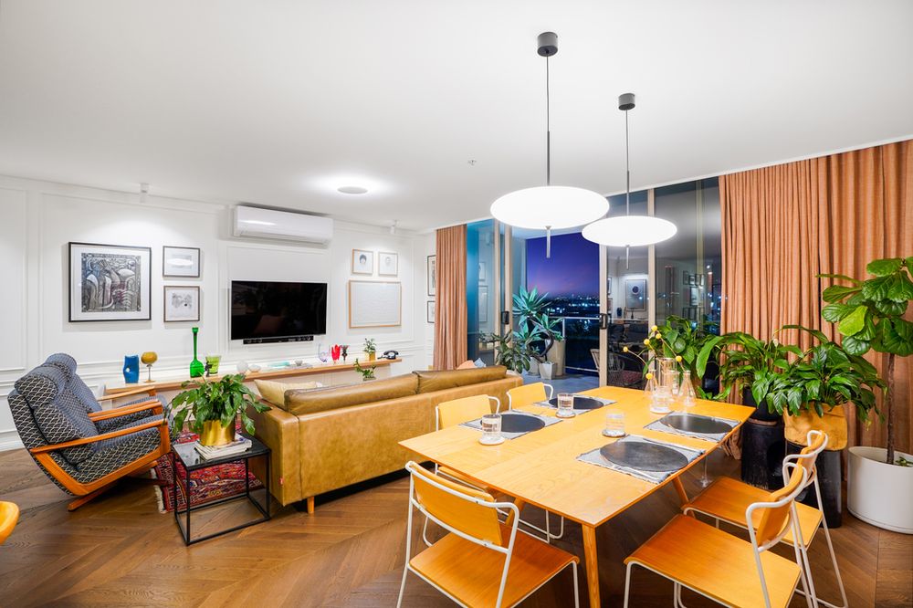Modern open-concept living room and dining area with warm wood floors and orange curtains overlooking city views.