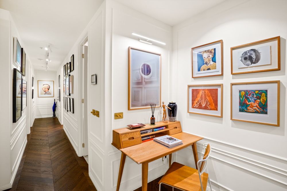 Elegant hallway gallery wall featuring colorful framed artwork and a wooden console table with chair.