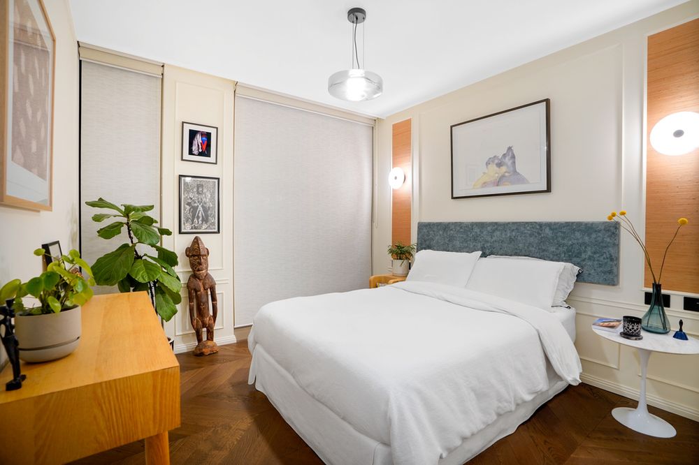 Cozy bedroom featuring white bedding, teal headboard, and wooden furnishings with modern decor accents.
