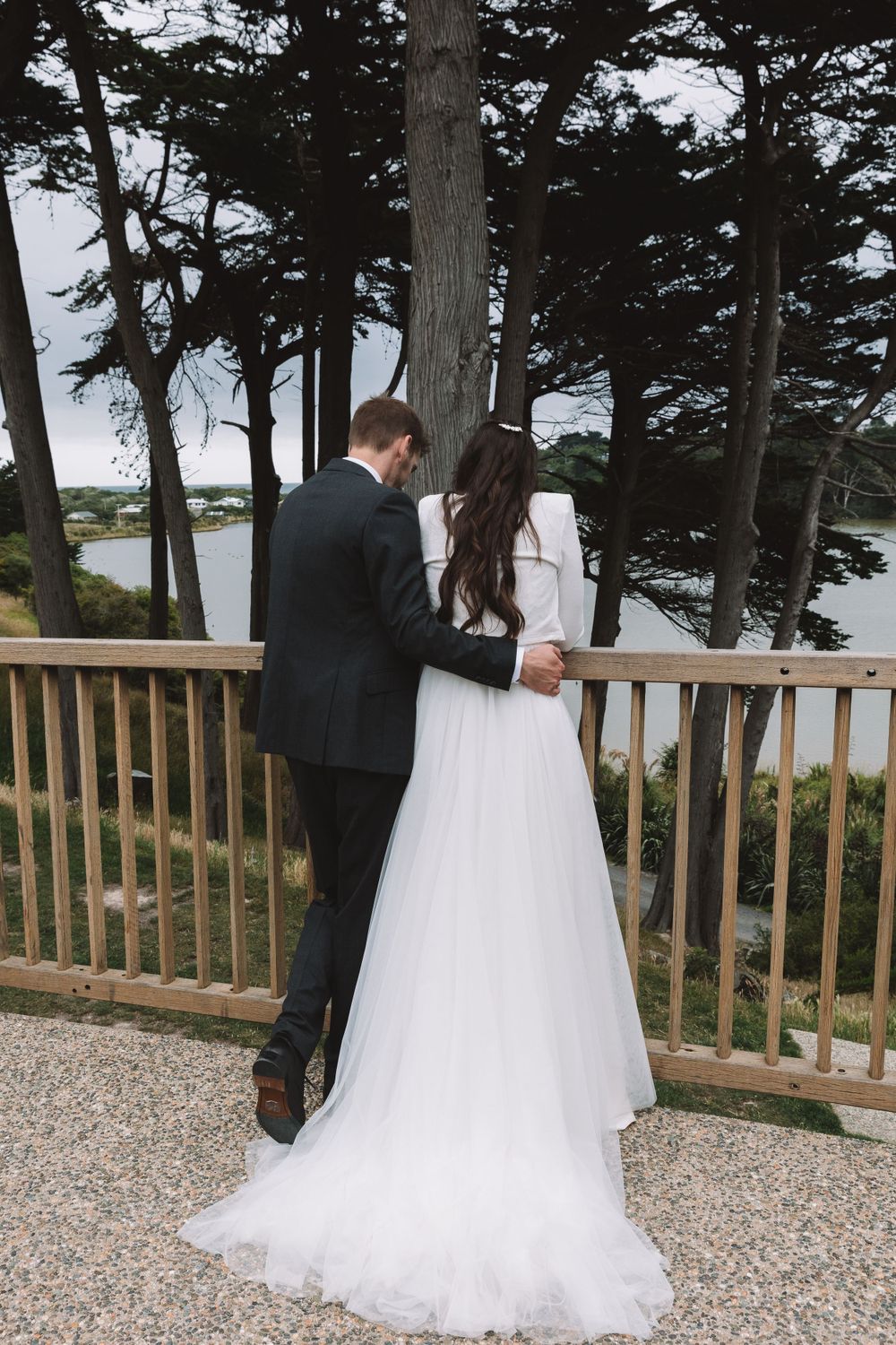 Couple shares romantic moment on wooden deck overlooking scenic water and pine trees.