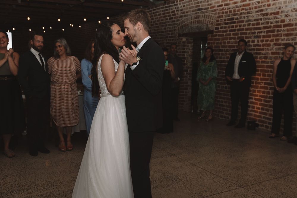 Couple shares their first dance in rustic brick venue with string lights overhead.