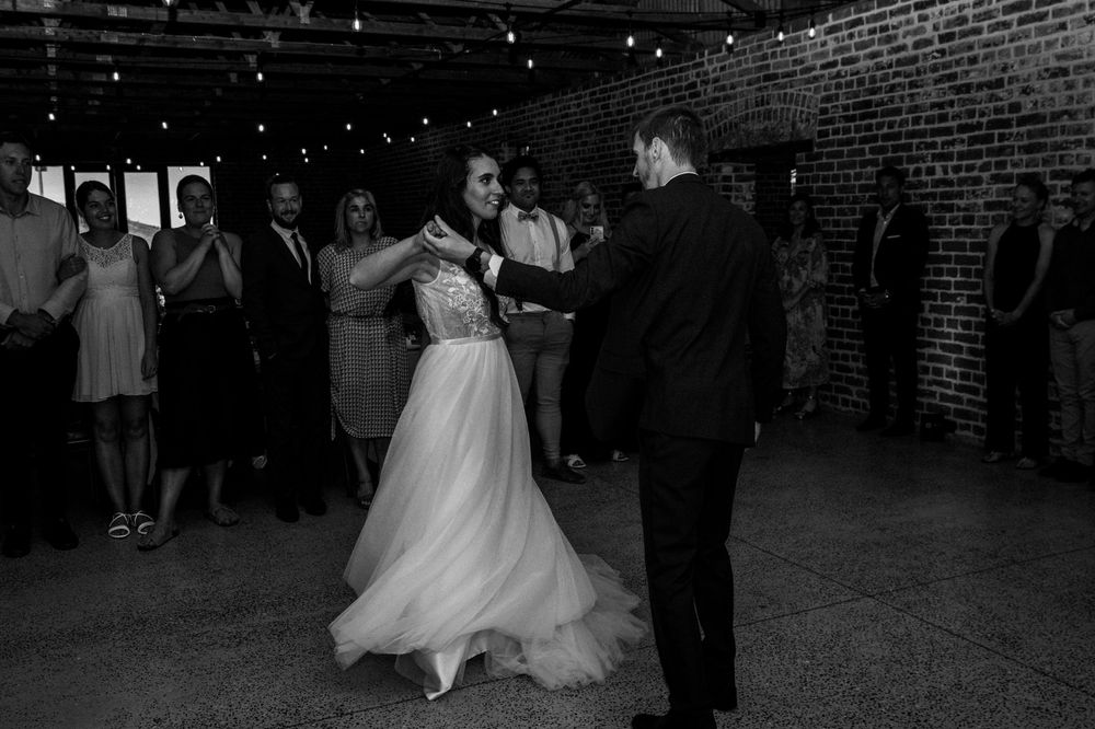 Black and white photo of couple dancing in rustic brick-walled reception venue.