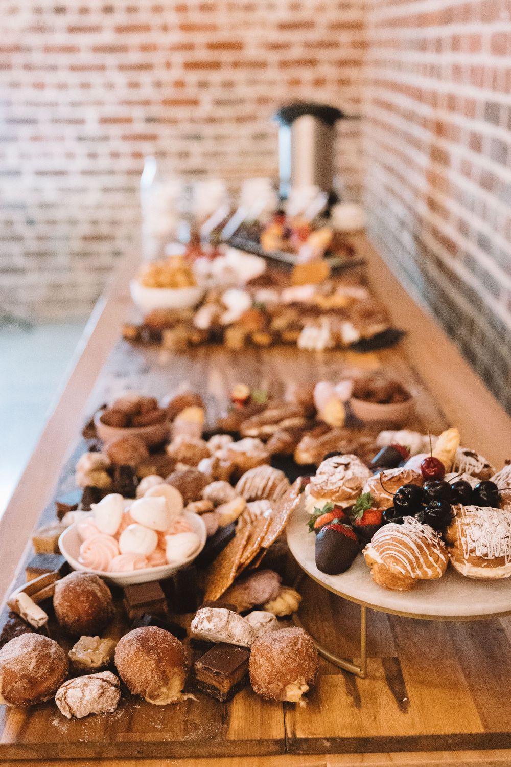 Various pastries and baked goods displayed on a rustic wooden table against exposed brick walls.