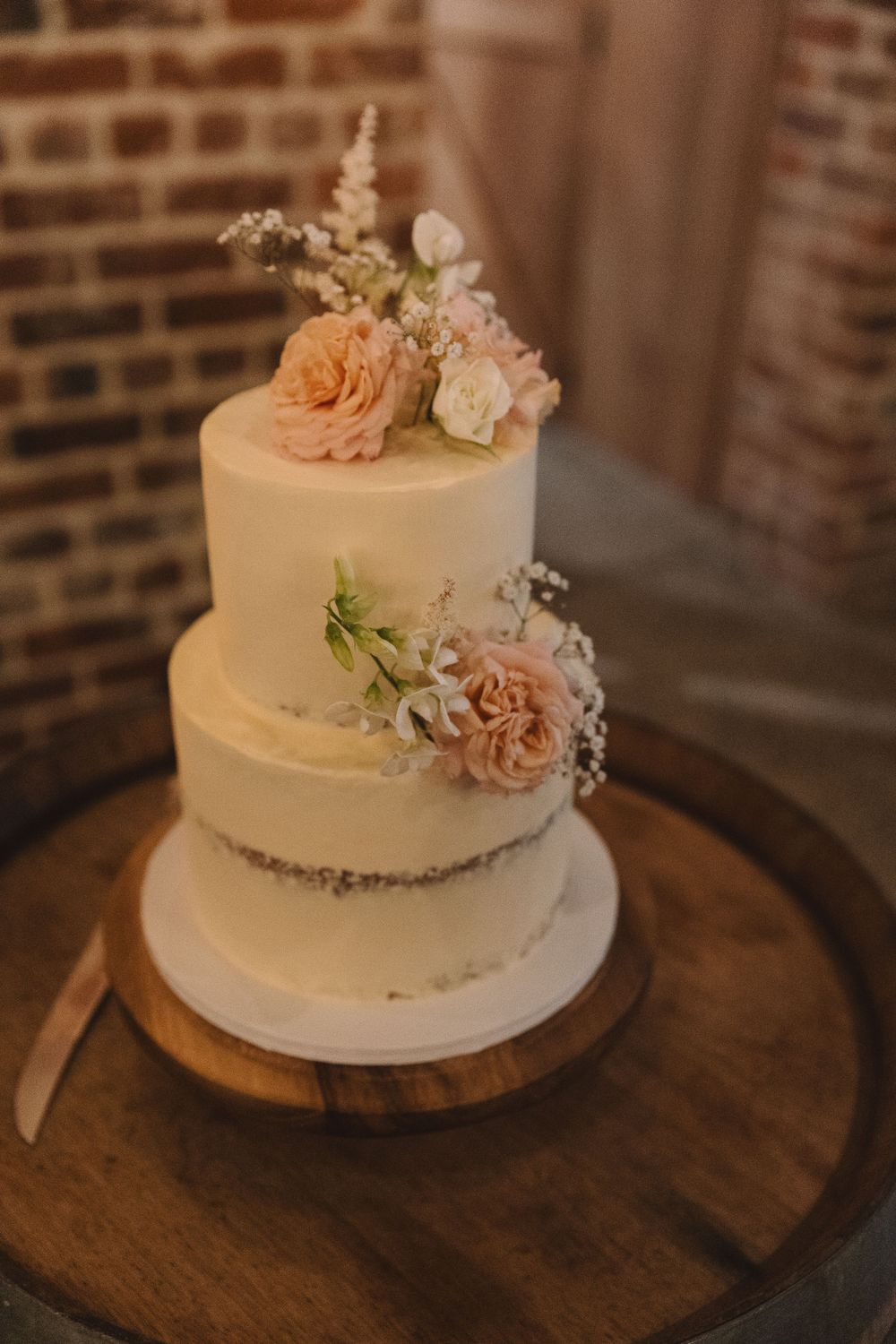 Elegant white wedding cake with peach roses and delicate floral accents on wooden display.