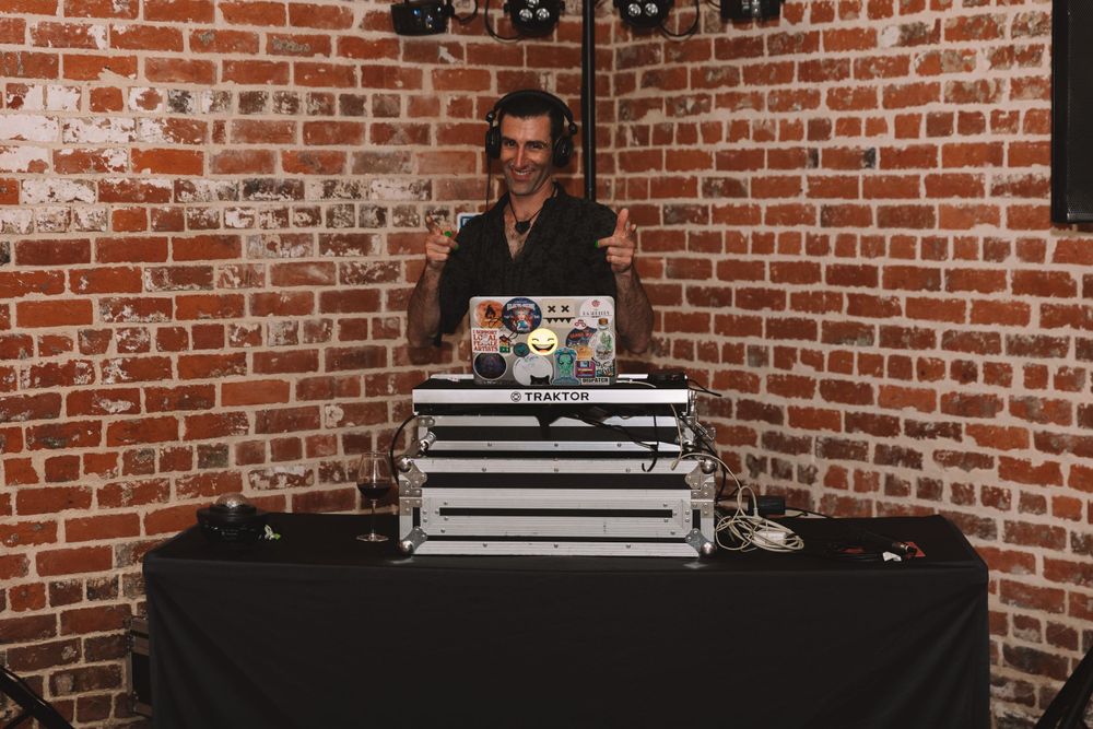 DJ setup with equipment on black table against exposed brick wall.