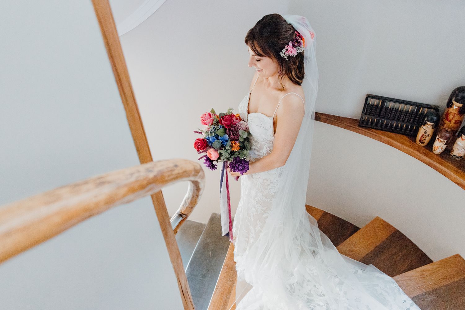 A stunning wedding dress showcased on a wooden staircase with a vibrant bouquet.