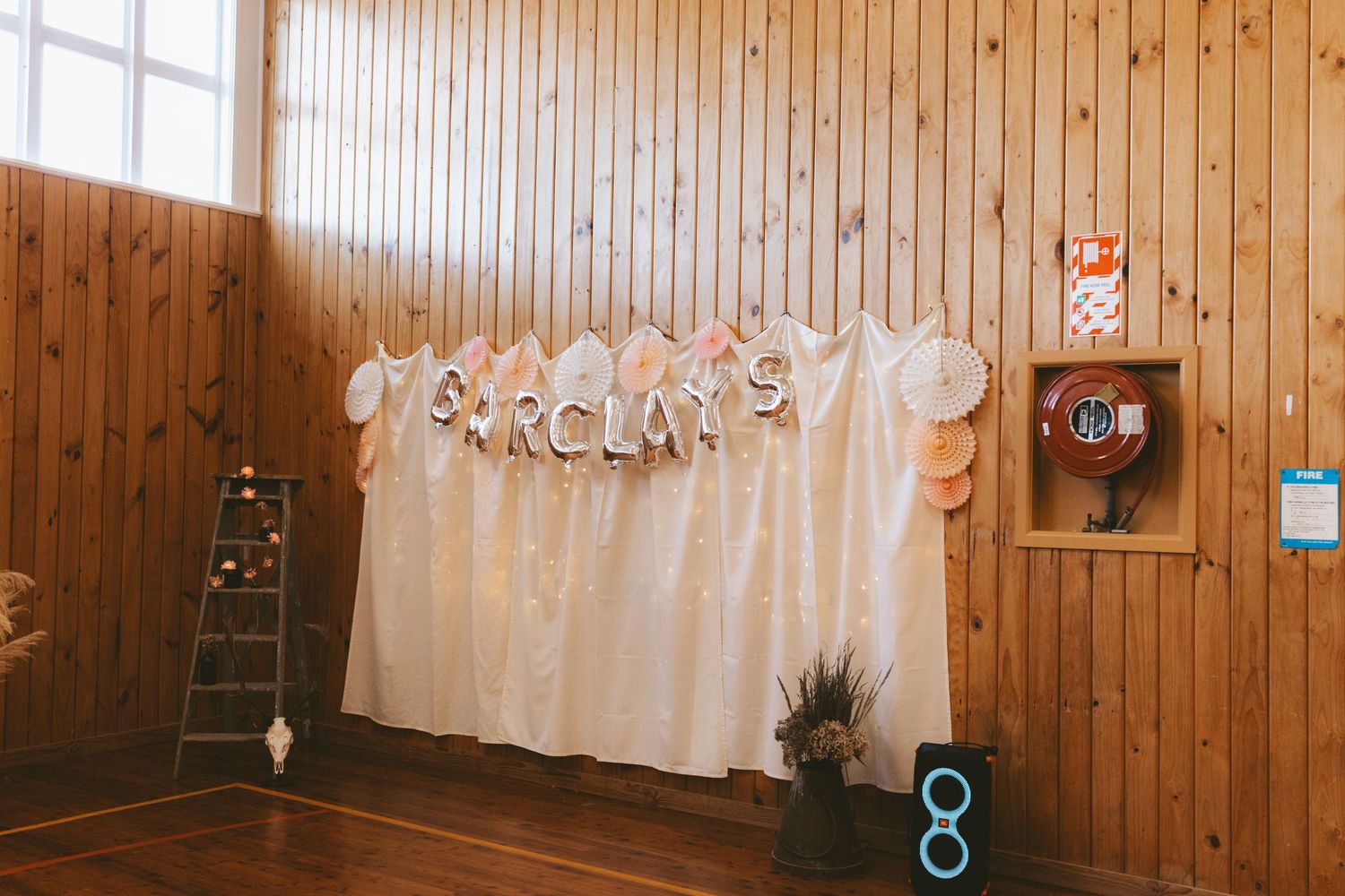 White balloon arch and curtain backdrop setup against wooden paneled walls for wedding reception.